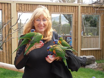 Valerie Blankhart. She is holding three exotic birds and smiling at the camera