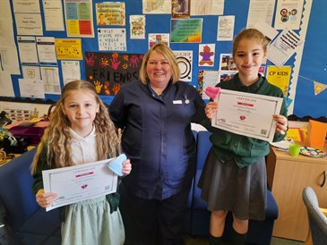 Violet Hawkins, Mel Mears and Olivia Frisby. They are pictured in a school office. The girls are wearing school uniform and holding certificates, Mel is in the centre in a nurses' uniform