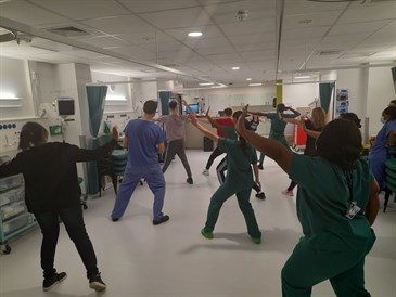 Zumba fun in the Elective Orthopaedic Centre. Photo shows a fitness class in progress in the recovery area of the elective orthopaedic centre. Staff are facing front, doing some dance moves. Photo is taken from behind.