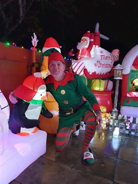 Paul Knight dressed as an elf with his Christmas lights display. Image shows Paul in an elf costume with some inflatable Christmas decorations