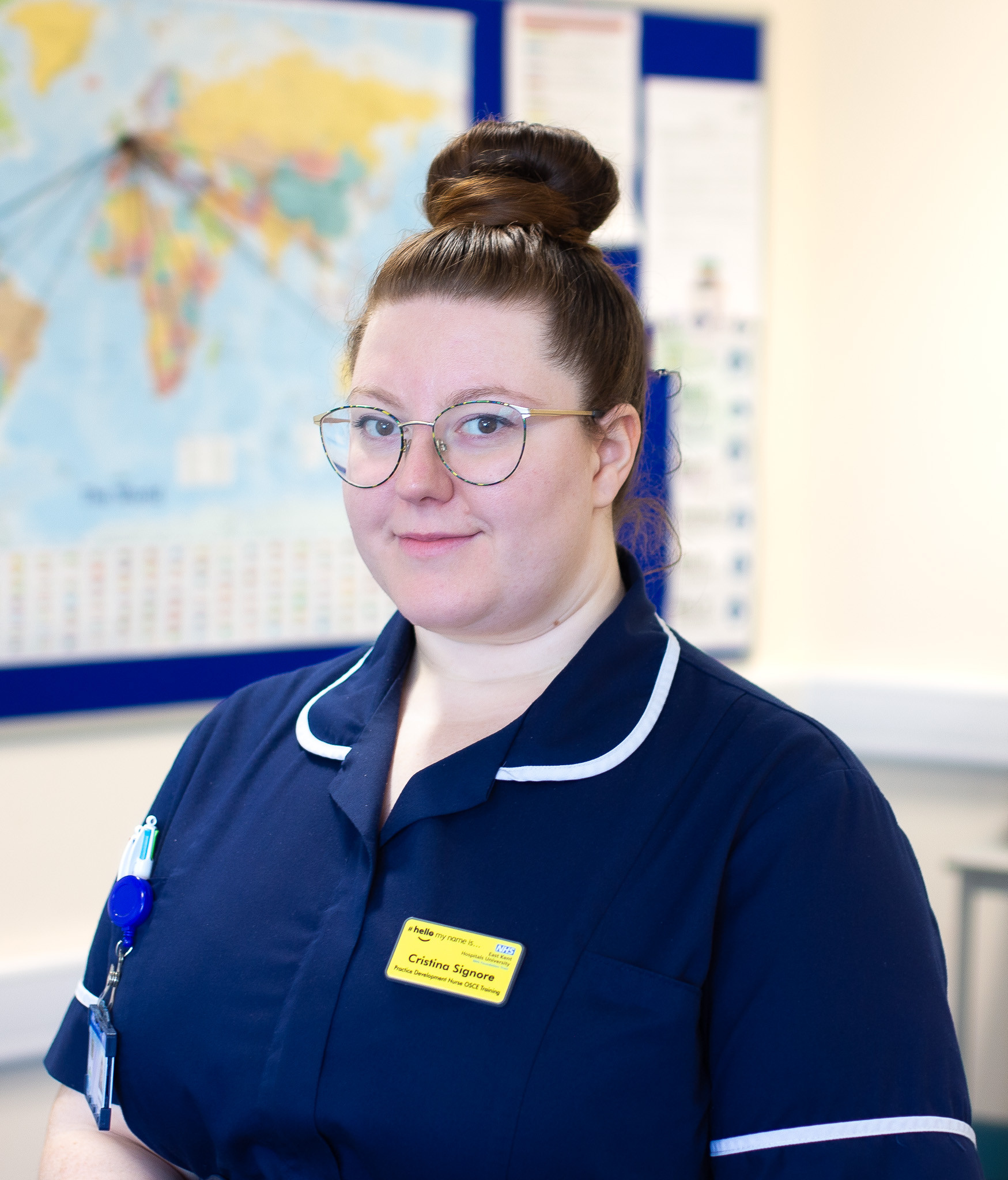 Cristina Signore. She is wearing a dark blue nurses' uniform with white trim and is looking at the camera. There is a map in the background