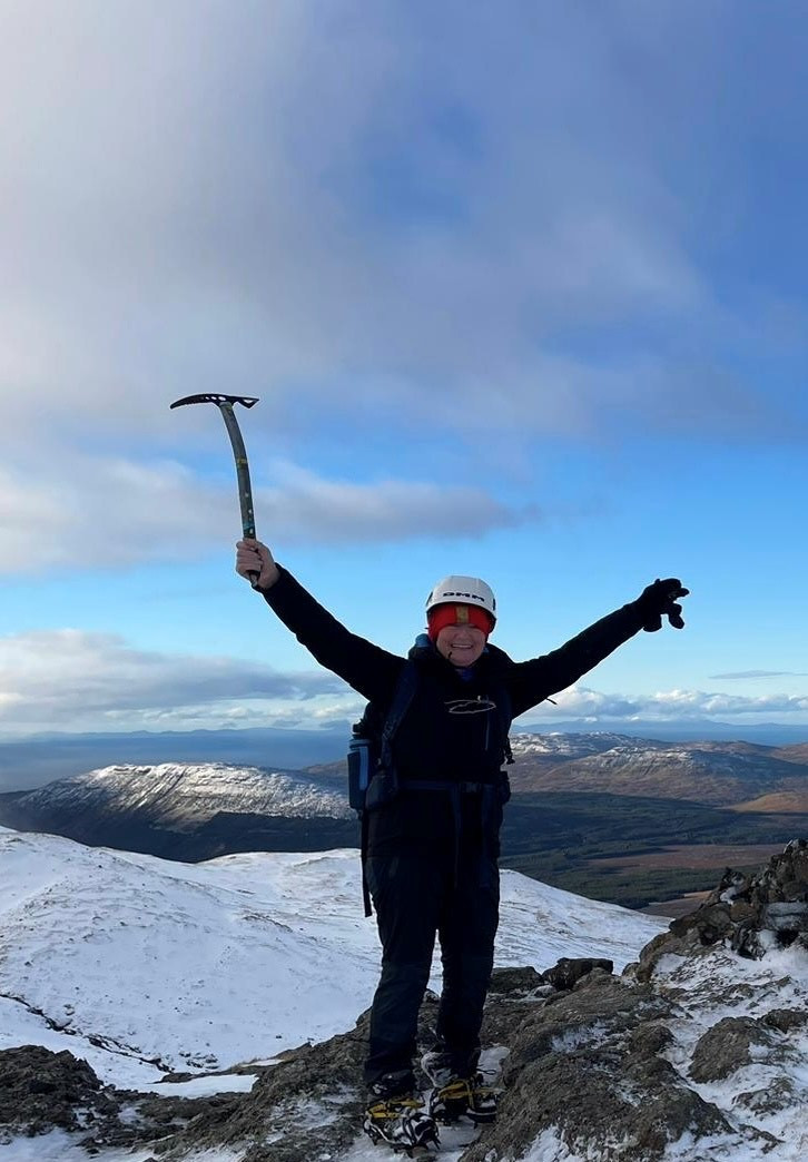 Jackie Crammond at the top of a snow-covered mountain with her arms in the air
