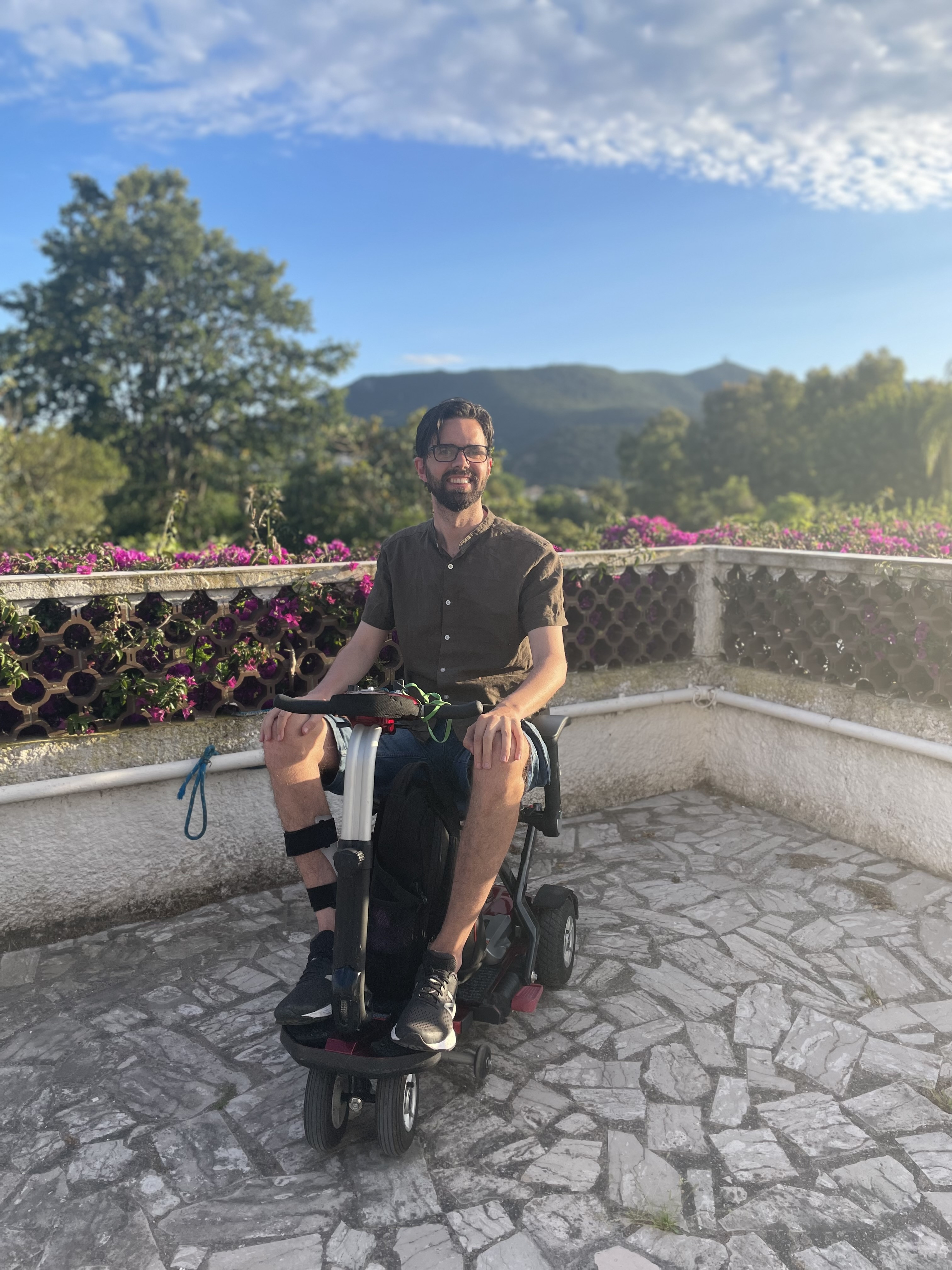 Jason enjoying one of his holidays. He is pictured on a mobility scooter with mountains and blue sky behind him