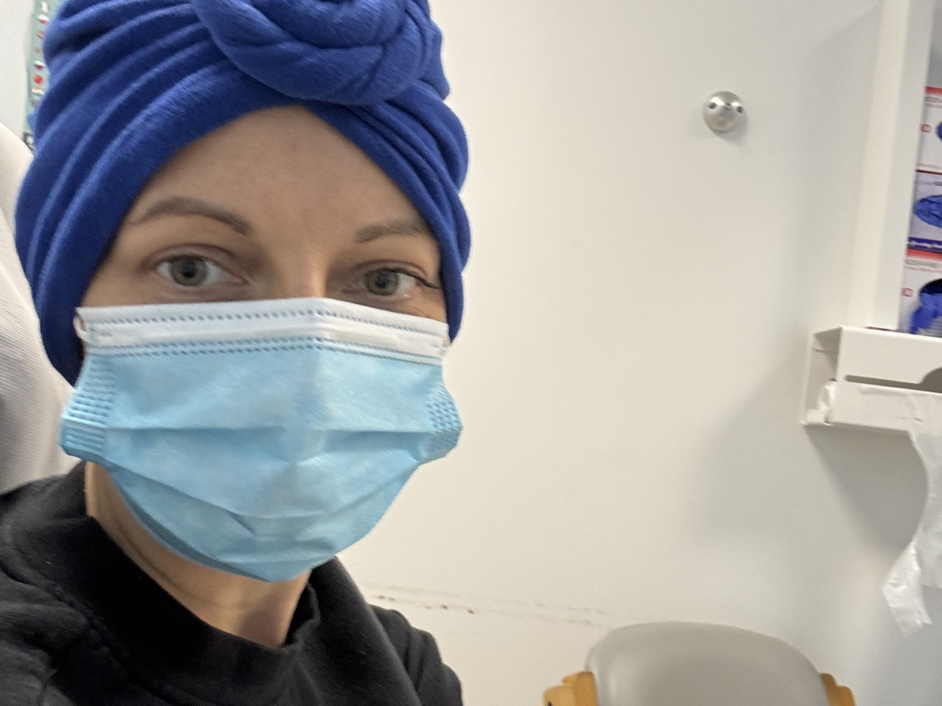 Natalie during her treatment. She is wearing a face mask and head scarf and has a cannula in her arm