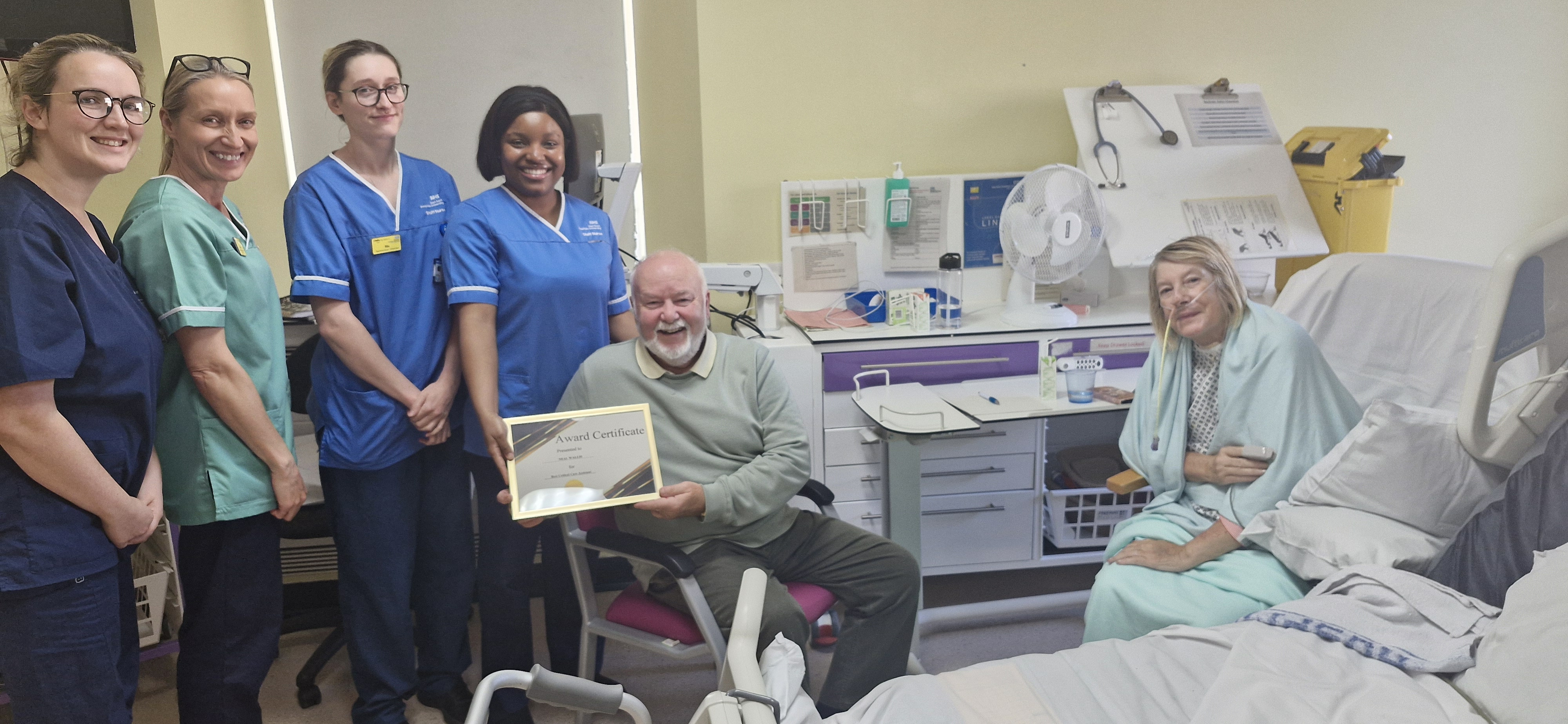 Neal shows off the certificate he received. He is pictured with staff and his wife, in a hospital chair
