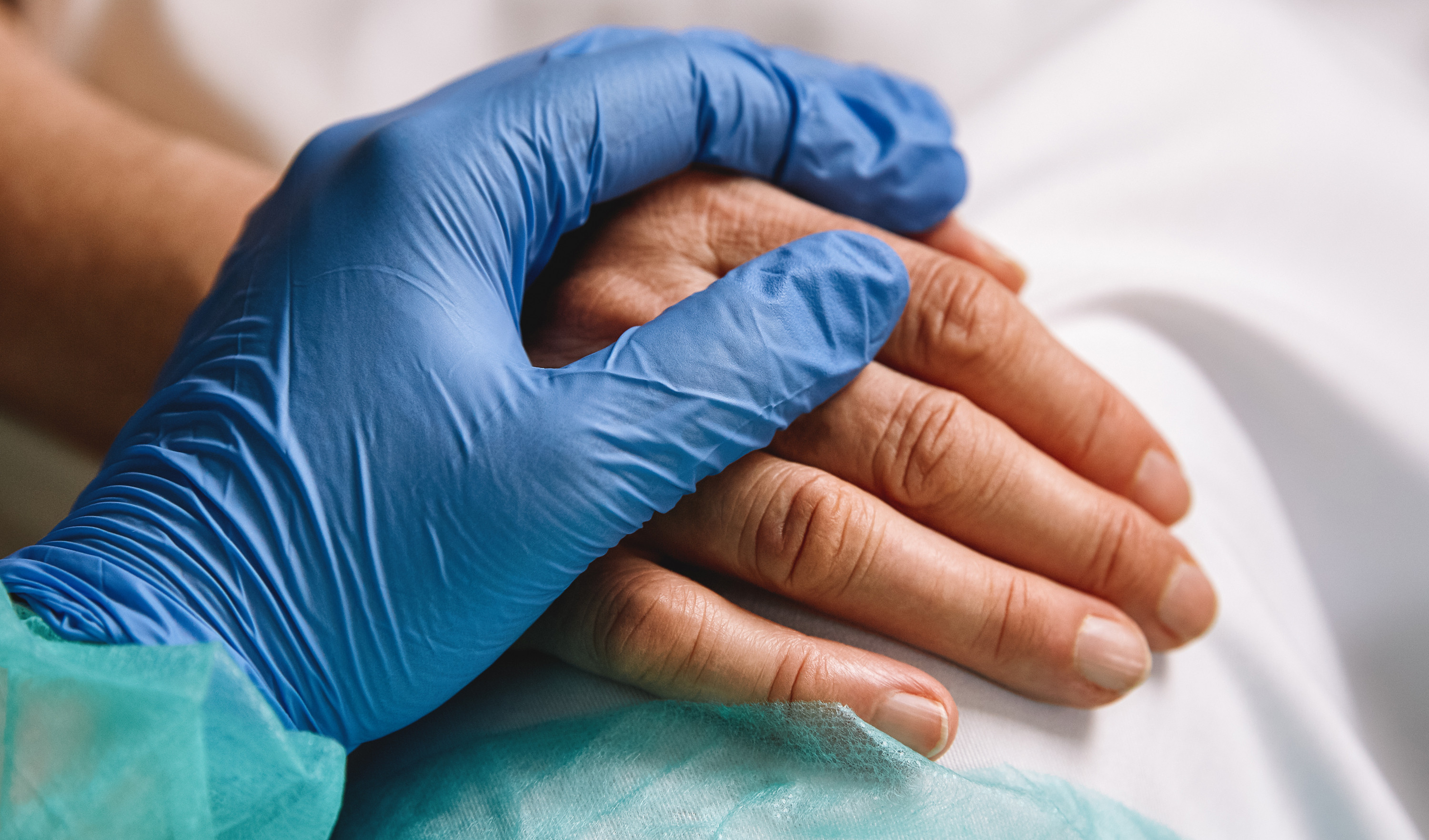 Gloved hand of nurse holding patient's hand