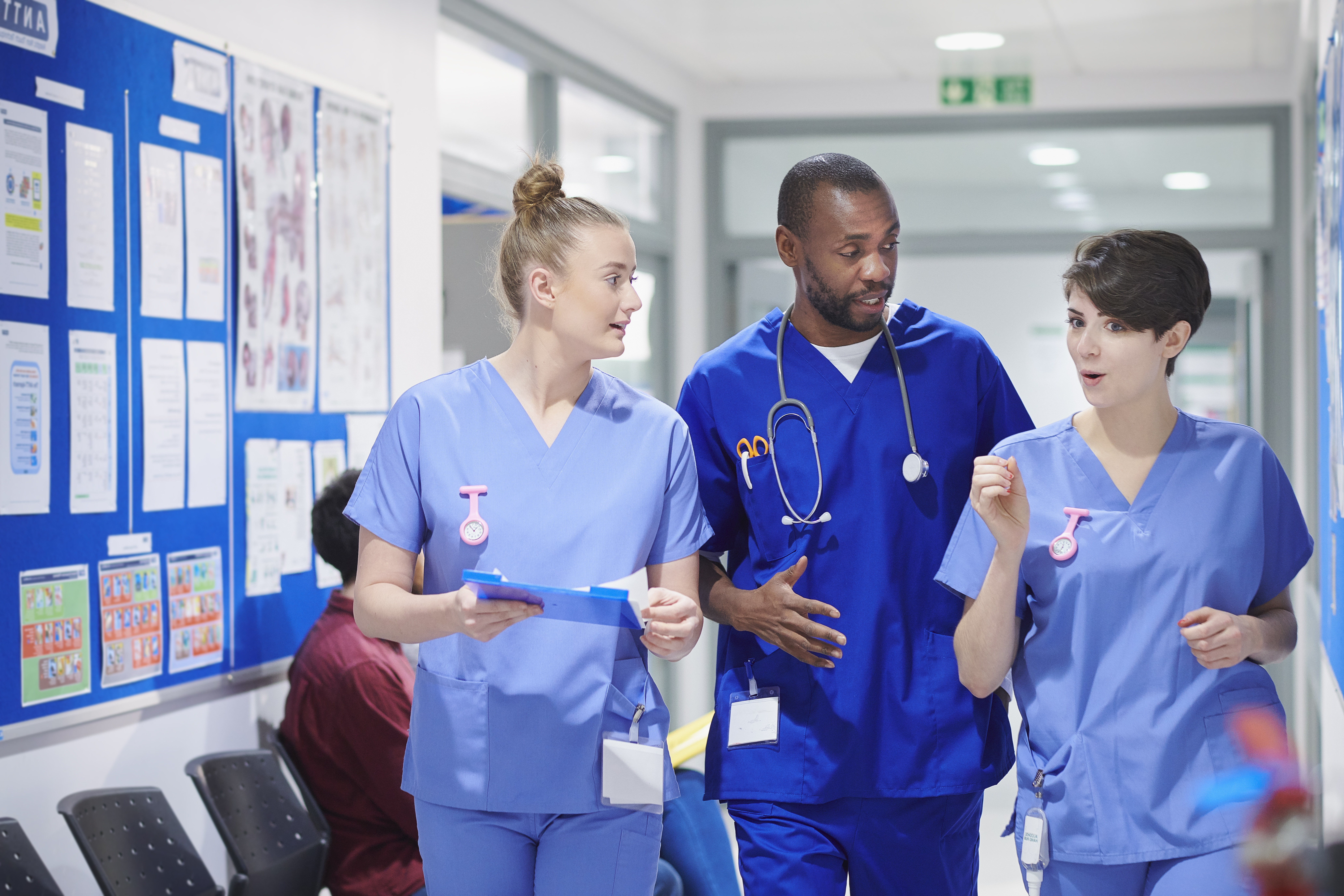 Two nurses and a doctor wearing scrubs, chatting in a corridor
